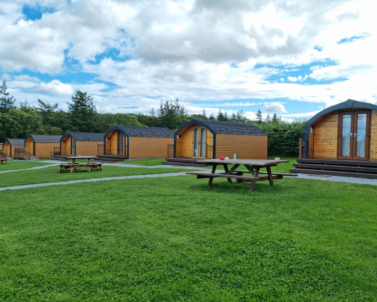 Timber glamping pods with picnic benches on the mown lawn at Greencraig